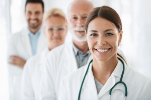Closeup front view of group of mixed age doctors at a hospital standing in a row and smiling at the camera. Mid 20's intern is in foreground with the rest of the team out of focus.